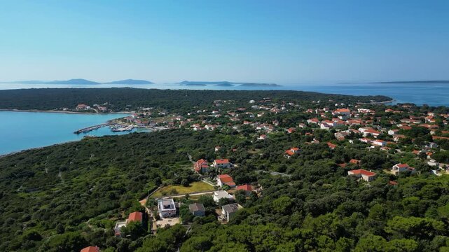 A breathtaking aerial drone panorama of old village on Silba Island, Croatia. The shot showcases the vibrant turquoise harbor, a docked ferry, and the charming coastal village stretching across the