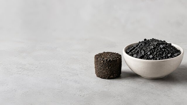 Biochar carbon removal concept shows White bowl filled with loose biochar and a compacted biochar on a gray surface.