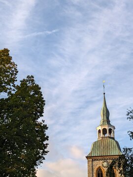 Church spire and treetop against sky with airplane contrails and chemtrails pattern