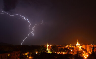 Intense electrical bolt striking down into the city horizon under heavy storm clouds © SebVoj
