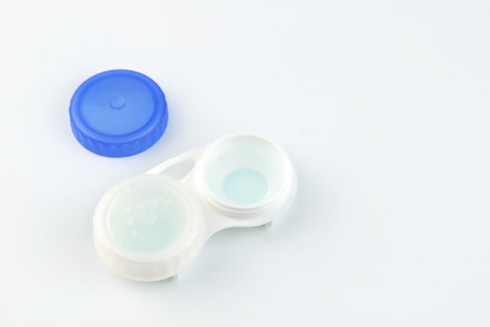 Close-up of contact lens case containing soft contact lenses soaking in solution with blue lid beside it.white background represents eye care,lens hygiene, vision correction and myopia nearsightedness