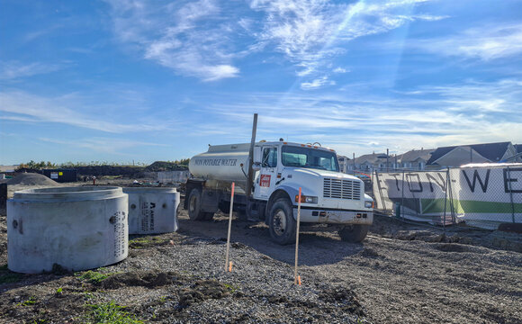 DIAMOND VALLEY, CANADA - 19 SEPTEMBER 2026: Potable water tank truck on residential construction site in Diamond Valley, Alberta, Canada with precast concrete utility structures