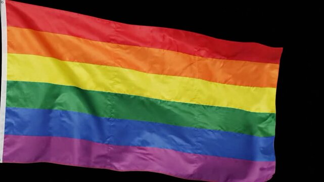 A gay pride rainbow flag waves slowly against a black background, celebrating unity and vibrant colors in slow motion