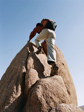 Determined Young Man Scaling Jagged Rocky Mountain Face Under Clear Blue Sky