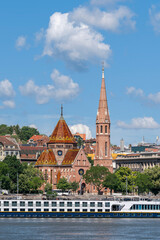 Fototapeta premium Red-brick Reformed church with a patterned tiled roof and tall spire standing beside the Danube embankment in Budapest