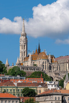 Tall Gothic Revival spire of Matthias Church rising above the tiled roof of the church and Fisherman's Bastion in Budapest