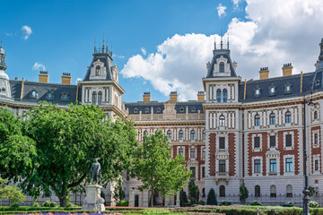 Ornate towers and brick facade of a railway administration palace seen beyond a garden and bronze statue in Budapest © Guillaume Angleraud