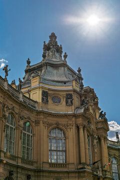 Sunlit baroque dome and curved facade of Vajdahunyad Castle with a crowned finial and flags in Budapest