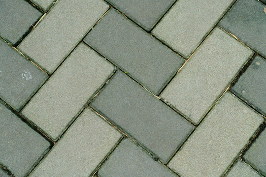 Top view of grey interlocking paving blocks pattern in herringbone style, outdoor ground texture background.