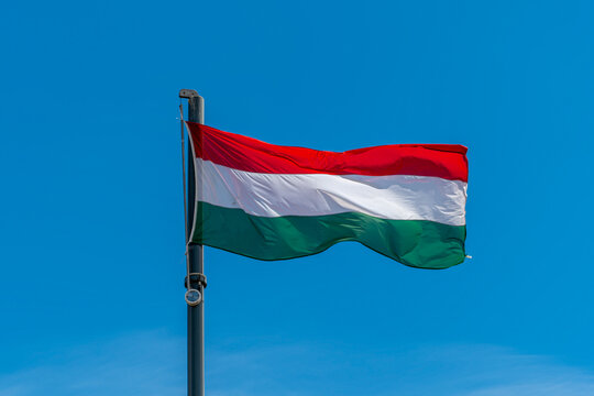 Hungarian national flag with red white and green horizontal stripes waving on a flagpole against a blue sky in Budapest, Hungary