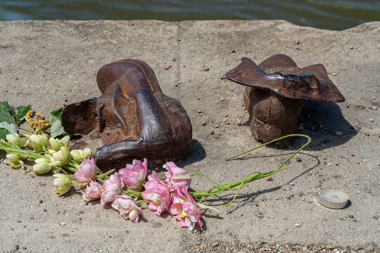 Two iron shoe sculptures with pink flowers and a candle on the stone edge of the Danube embankment in Budapest, Hungary