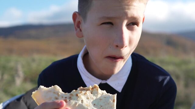 Picnic, eating, teenager, boy enjoying a satisfying outdoor meal or snack in a scenic mountain field during sunny daylight