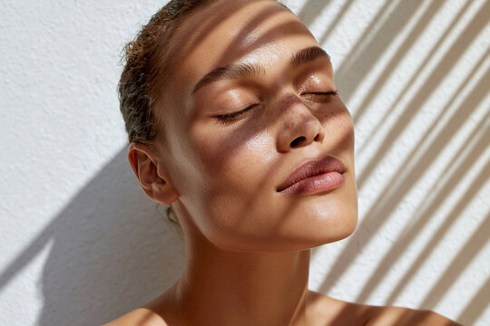 Young woman basking in sunlight with eyes closed and patterned shadow across face