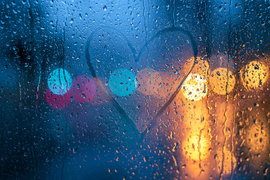 Modern love background with heart on fogged rainy window and colorful urban bokeh