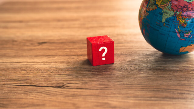Red question mark block next to world globe on wooden background global uncertainty international business question concept
