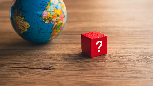 Red question mark block beside planet earth globe on wooden table international market strategy global decision concept