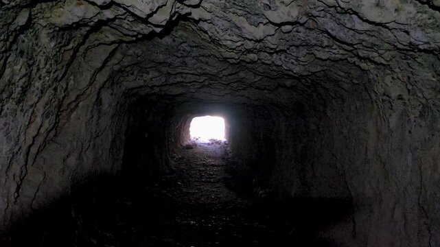 Camera smoothly zooming in on the bright exit light at the end of a dark cave rock tunnel.