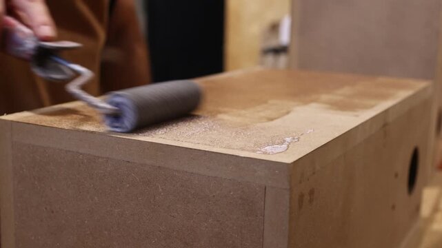 Carpenter applying varnish to mdf box with roller