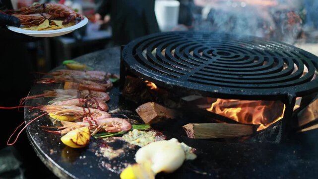 Shrimp grilling on round charcoal grill with lemon slices and garlic sauce. Barbecue seafood cooking over burning wood and coals, outdoor summer food preparation concept.