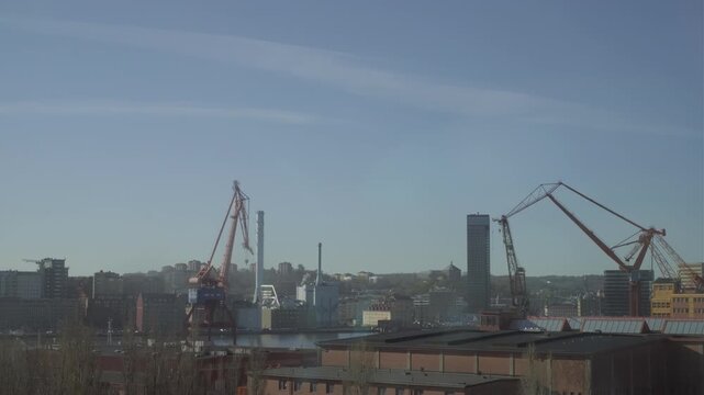 Gothenburg, Sweden - May 2 2023: Two industrial harbor cranes rise above the Gothenburg skyline in hazy morning light, with a high-rise tower and city rooftops visible along the waterfront