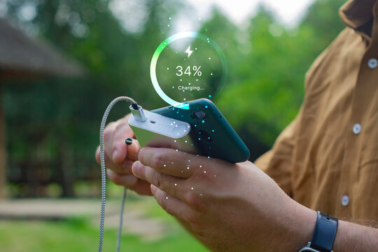 Person holding smartphone connected to power bank outdoors with battery charging percentage HUD overlay. Portable energy charger, fast charging technology and mobile battery supply concept.