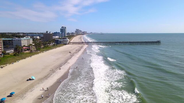 Beyond scattered beachgoers, pier pilings extend into Atlantic water along Myrtle Beach.
