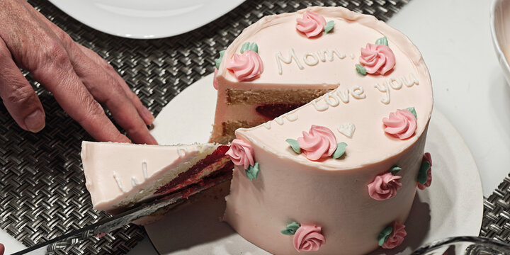 Hand serving a piece of a delicately homemade pink cake adorned with intricate roses and the words Mom, we adore you, commemorating a special and sweet occasion