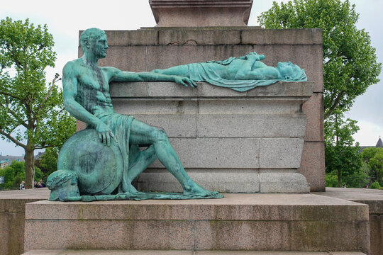 The bronze sculpture group at the base of the G&euml;lle Frau war memorial in Luxembourg City, depicting a seated bronze soldier mourning a fallen comrade lying atop a stone plinth.