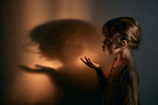 The silhouette of a playing child is cast against a wall bathed in warm light.space on the side for text.a faint warm glow suggesting candlelight bleeding into the shadow's edge