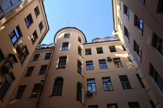Well courtyard enclosed by beige apartment buildings; a modern glass-paneled structure juts into the frame, contrasting with historic architecture
