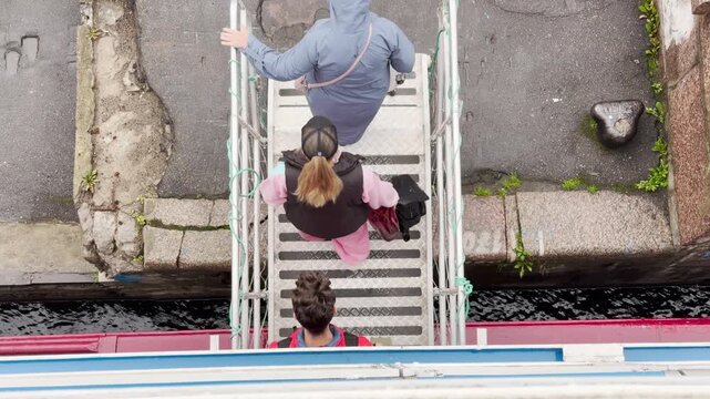 Passengers walk down a metal gangway onto the pier. They disembark happily from a cruise ship on the Neva River in Saint Petersburg. The arrival brings eager joy and hope.