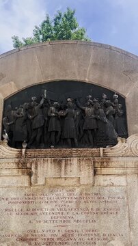 Vertical close-up of a bronze relief on the Giuseppe Verdi Monument in Parma, Italy, depicting the 1859 Italian unification plebiscite and a crowd of delegates.