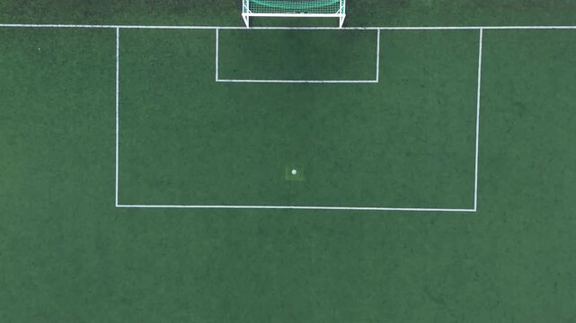Straight-down drone view of a football penalty area with netted goal, six-yard box, penalty spot and clean white markings on green synthetic turf.