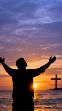 Silhouette of a Man Praying and Worshipping at Sunset on a Beach with a Cross