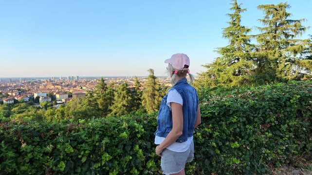 Woman standing on a hill viewing panoramic cityscape of Bologna, Italy, with historic architecture, including famous Two Towers, and Basilica Saint Petronius, dedicated to patron saint of Bologna.