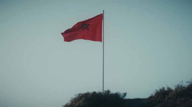 The Moroccan flag waves atop a flagpole against a clear sky in Tamraght, Morocco.