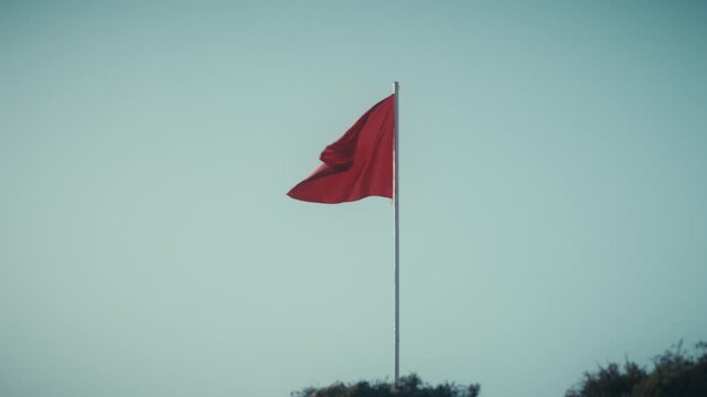 The Moroccan flag waves atop a flagpole against a clear sky in Tamraght, Morocco.