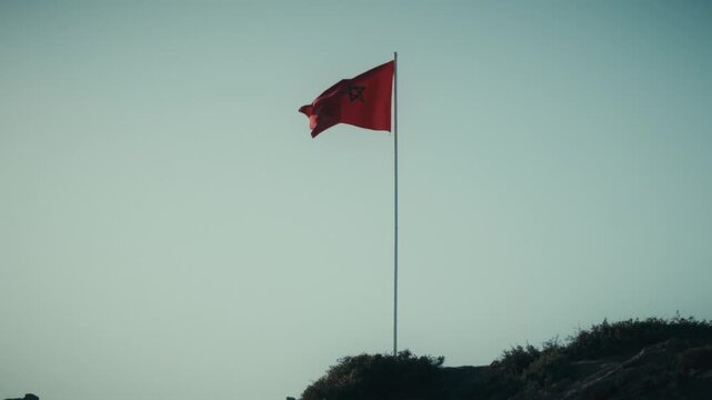 The Moroccan flag waves atop a flagpole above the coastline at dusk in Tamraght, Morocco.