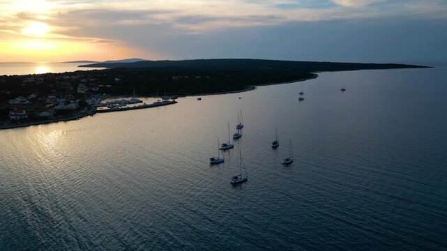 A stunning aerial drone shot capturing the warm golden sunset over the Sotorisce bay and Mulj harbor area on Silba Island, Croatia. The perspective showcases the sheltered marina filled with boats