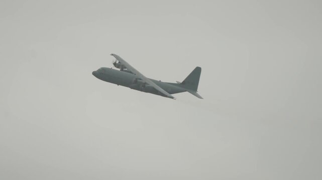 Dutch air force Hercules military transport aircraft banks through overcast sky during Falcon Leap paratrooper exercise near Oosterbeek Netherlands in tracking telephoto shot.
