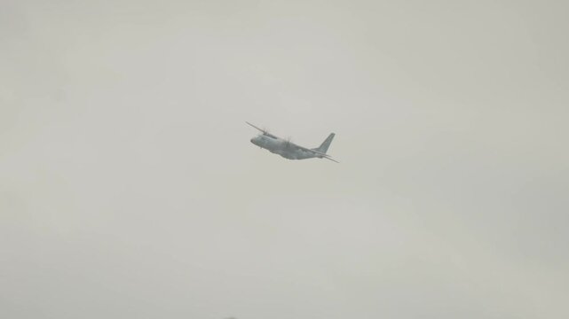 Polish Air Force tactical transport plane climbs through misty overcast skies during Falcon Leap airborne event near Oosterbeek Netherlands in smooth panning telephoto view.