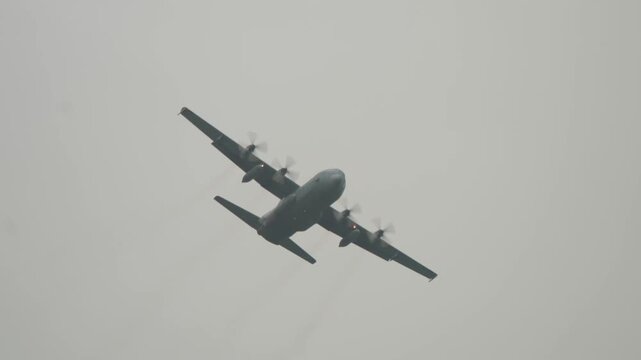 Low angle tracking shot following tactical military transport airplane gliding across gloomy overcast sky during Falcon Leap airborne exercise commemoration.