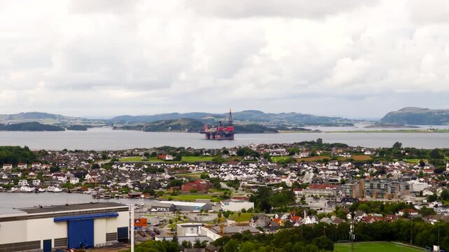 Aerial view, Stavanger, Norway, showing an offshore heavy lift crane vessel in the fjord beyond a coastal urban area, highlighting marine engineering and offshore industry