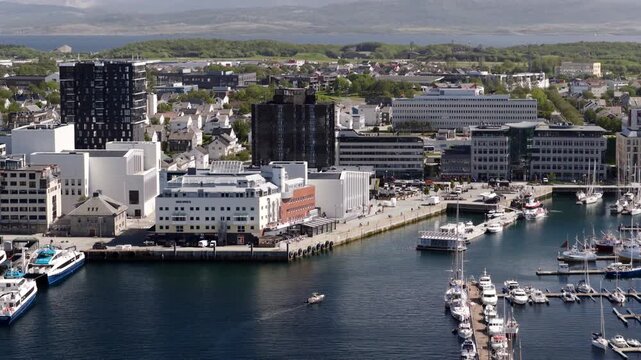 Vessel cruises into Bodo harbor with buildings on waterfont. Aerial view