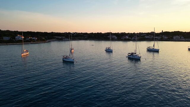 A stunning aerial drone shot capturing the warm golden sunset over the Sotorisce bay and Mulj harbor area on Silba Island, Croatia. The perspective showcases the sheltered marina filled with boats