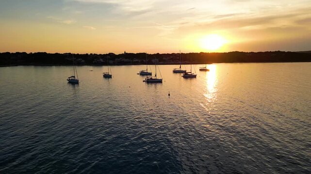 A stunning aerial drone shot capturing the warm golden sunset over the Sotorisce bay and Mulj harbor area on Silba Island, Croatia. The perspective showcases the sheltered marina filled with boats
