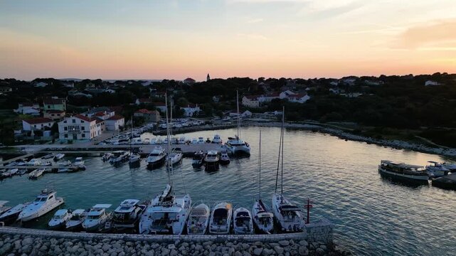 A stunning aerial drone shot capturing the warm golden sunset over the Sotorisce bay and Mulj harbor area on Silba Island, Croatia. The perspective showcases the sheltered marina filled with boats