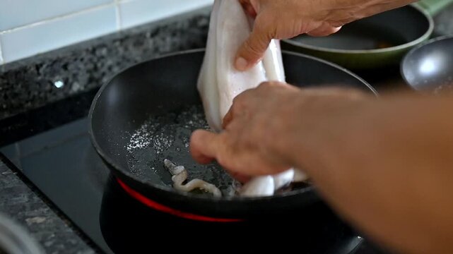 Hands placing fresh squid into a hot pan with olive oil and adding sea salt, seafood preparation, Mediterranean cooking, seasoning technique, fresh ingredients, homemade food and culinary process