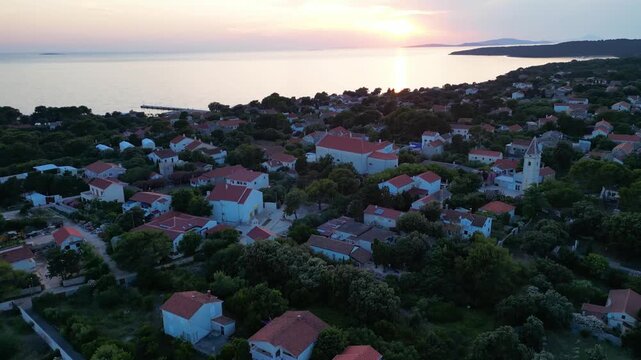 A breathtaking evening aerial drone panorama of old village on Silba Island, Croatia. The shot showcases the vibrant turquoise harbor, a docked ferry, and the charming coastal village stretching