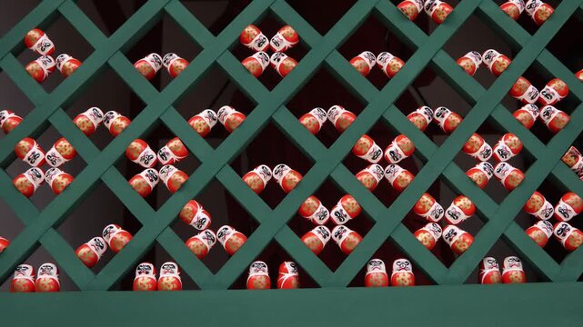 Traditional red Daruma dolls arranged behind a decorative lattice at Katsuo-ji Temple in Minoh, Osaka, Japan, creating a striking geometric pattern associated with luck and perseverance